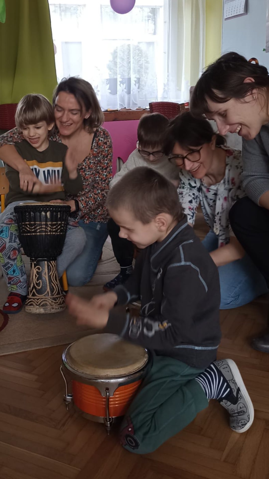 Dzieci grają na bębnach, a dorośli z uśmiechami obserwują dzieci