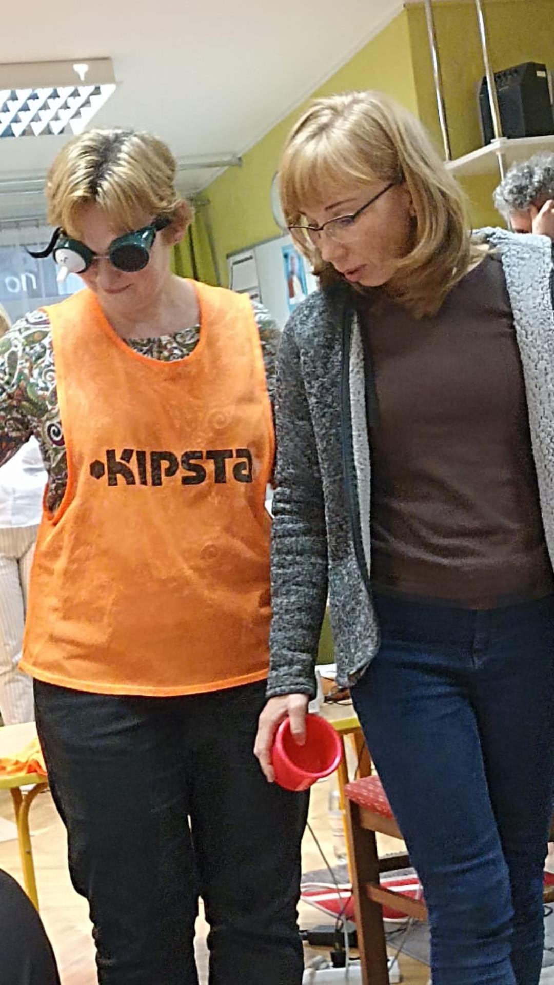 Pani Monika prowadzi panią Beatę, która ma założony symulator widzenia.