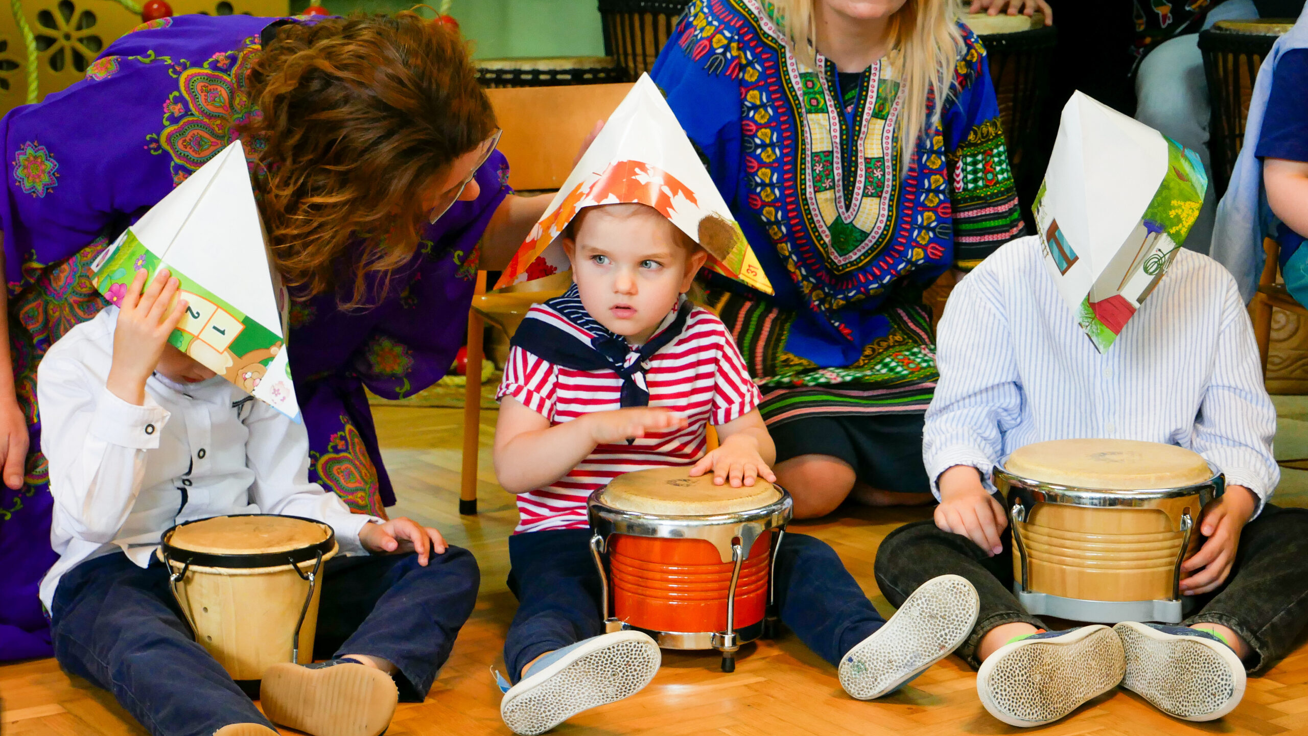 Dzieci grają na bębnach. Na głowach mają trójkątne czapki z papieru.