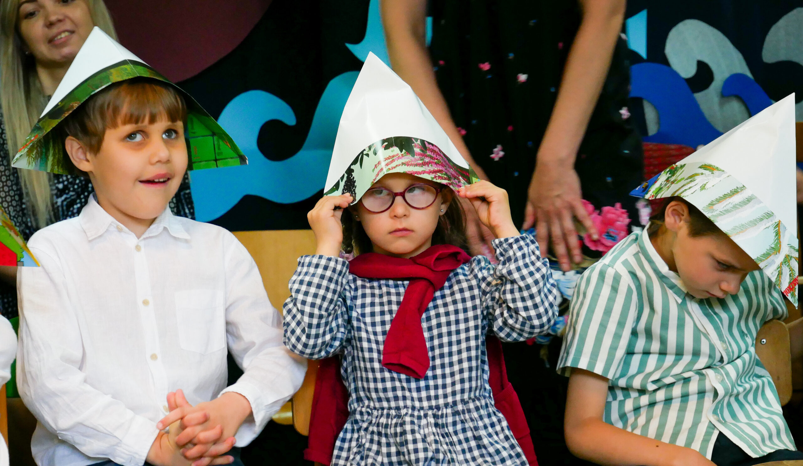 Dzieci w trójkątnych czapkach z papieru.