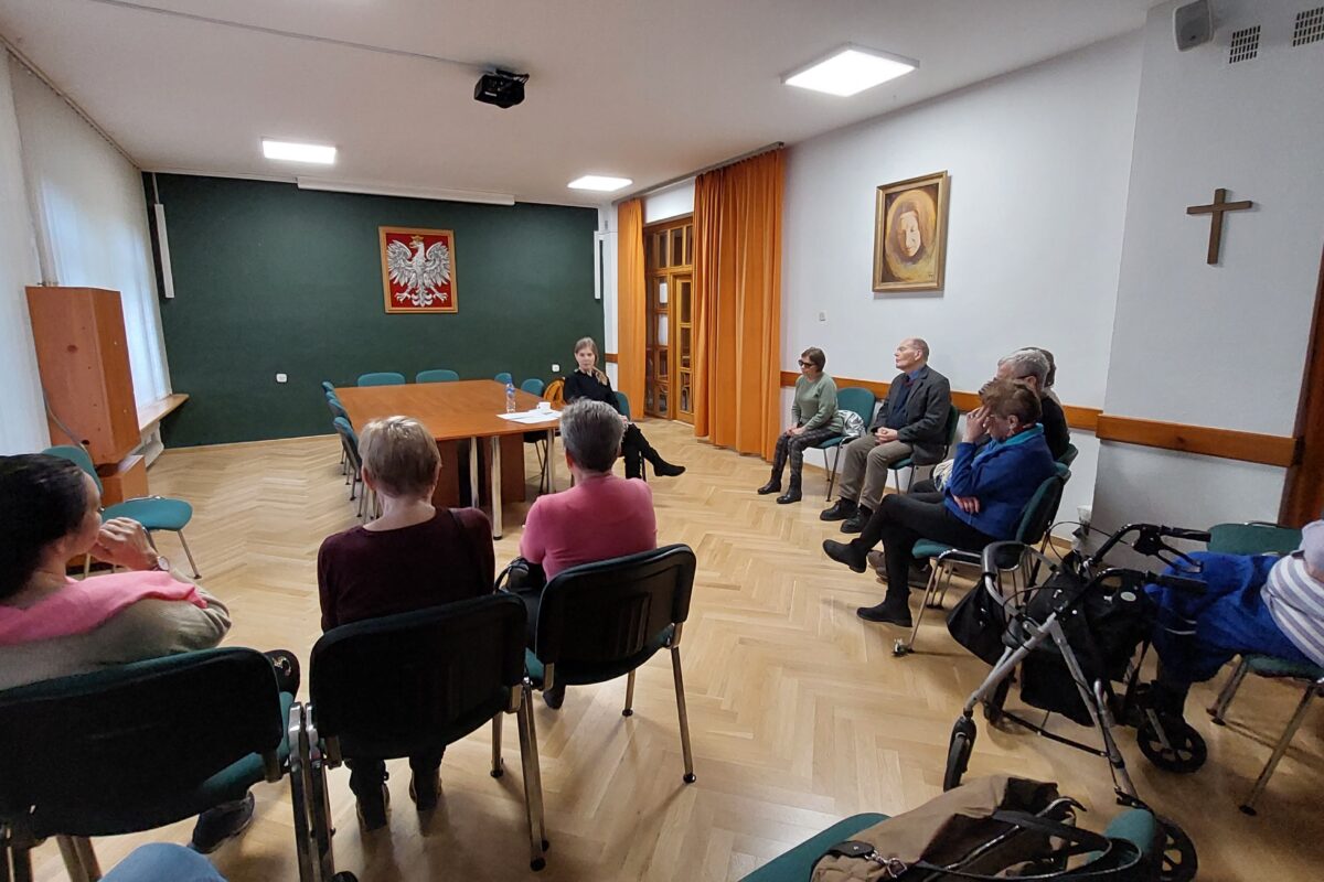 Seniorzy zebrani na sali konferencyjnej słuchają wykładu.