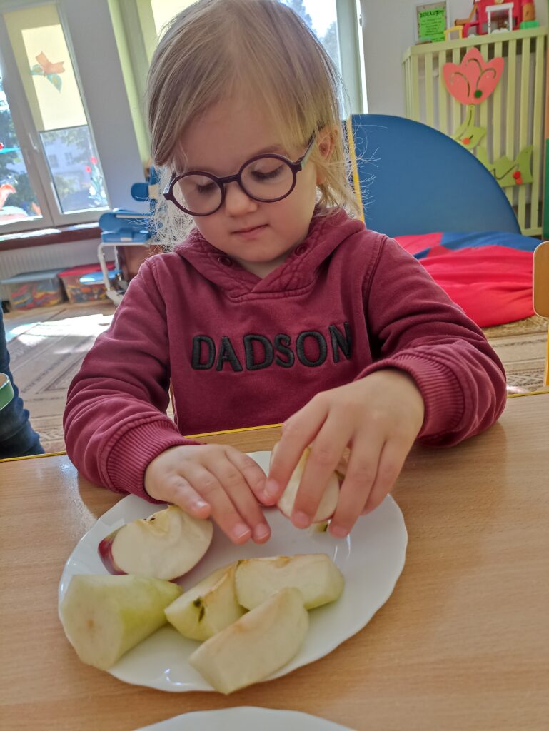 Dziewczynka ogląda pokrojone w ćwiartki obrane jabłka.