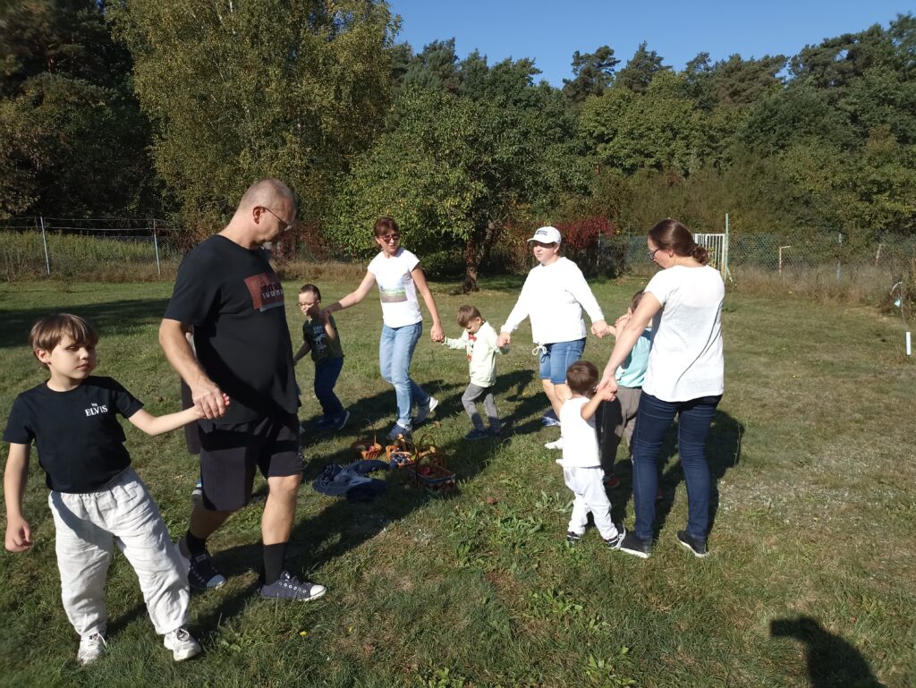 Dzieci i nauczyciele bawią się w kole w sadzie.