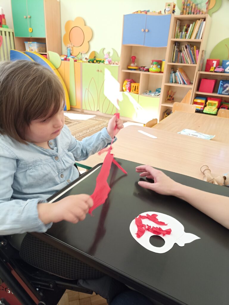 Dziewczynka rozrywa bibułę. Wykleja nią papierowy kształt jabłka.