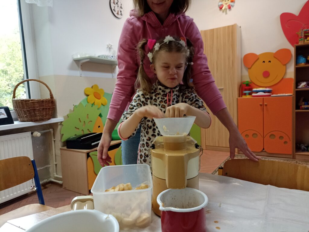 Dziewczynka wkłada owoce do sokowirówki.