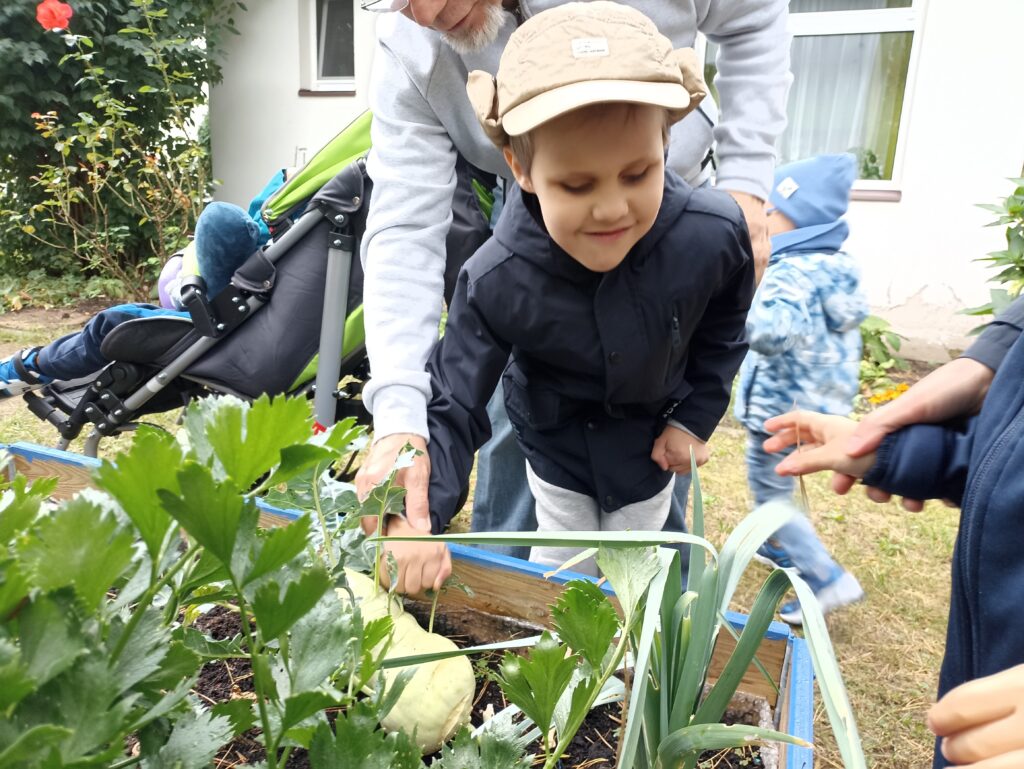 Uśmiechnięty chłopiec stoi przy skrzyni w ogrodzie.