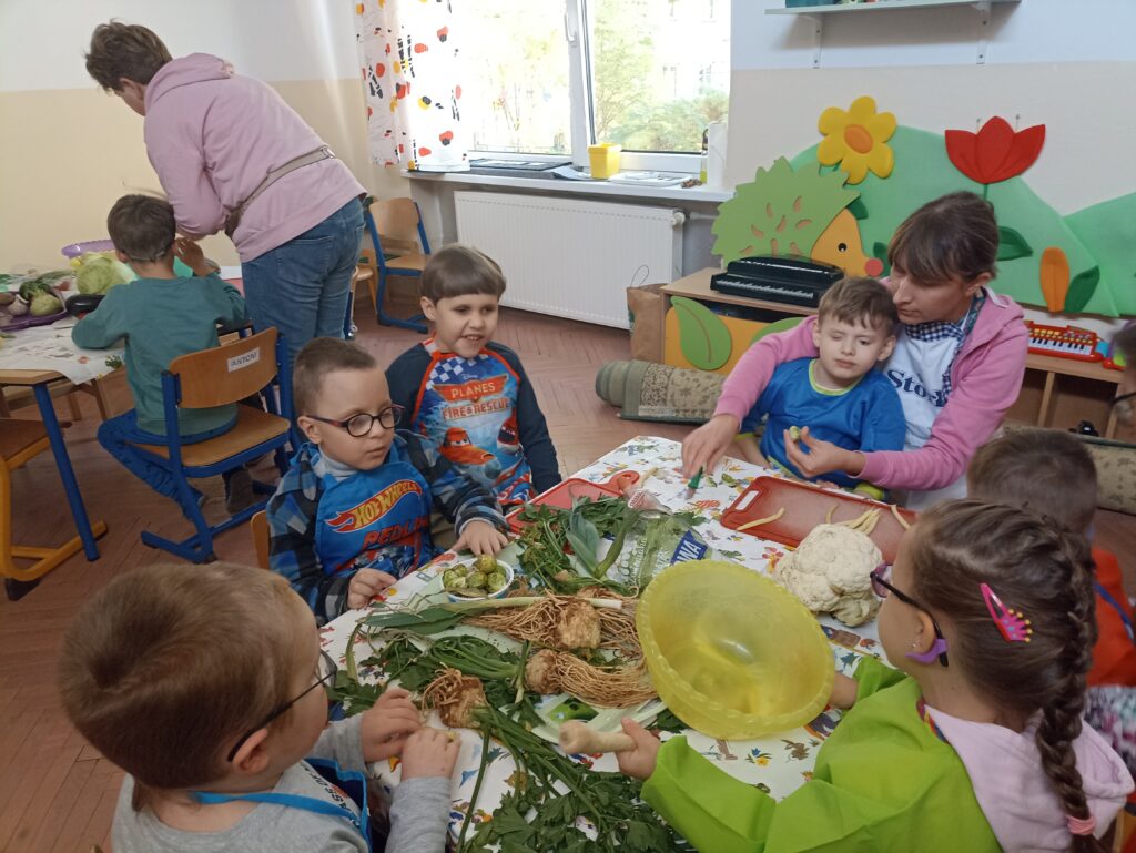 Chłopcy siedzą przy stole i kroją warzywa.