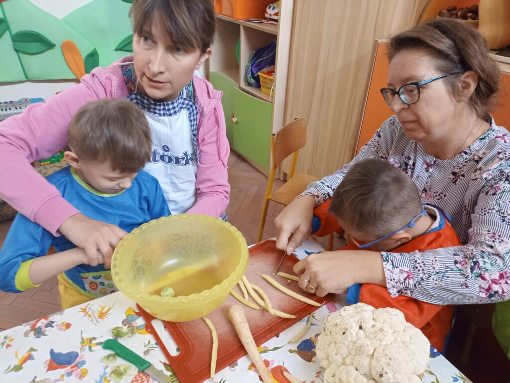 Dzieci z Paniami kroją warzywa.