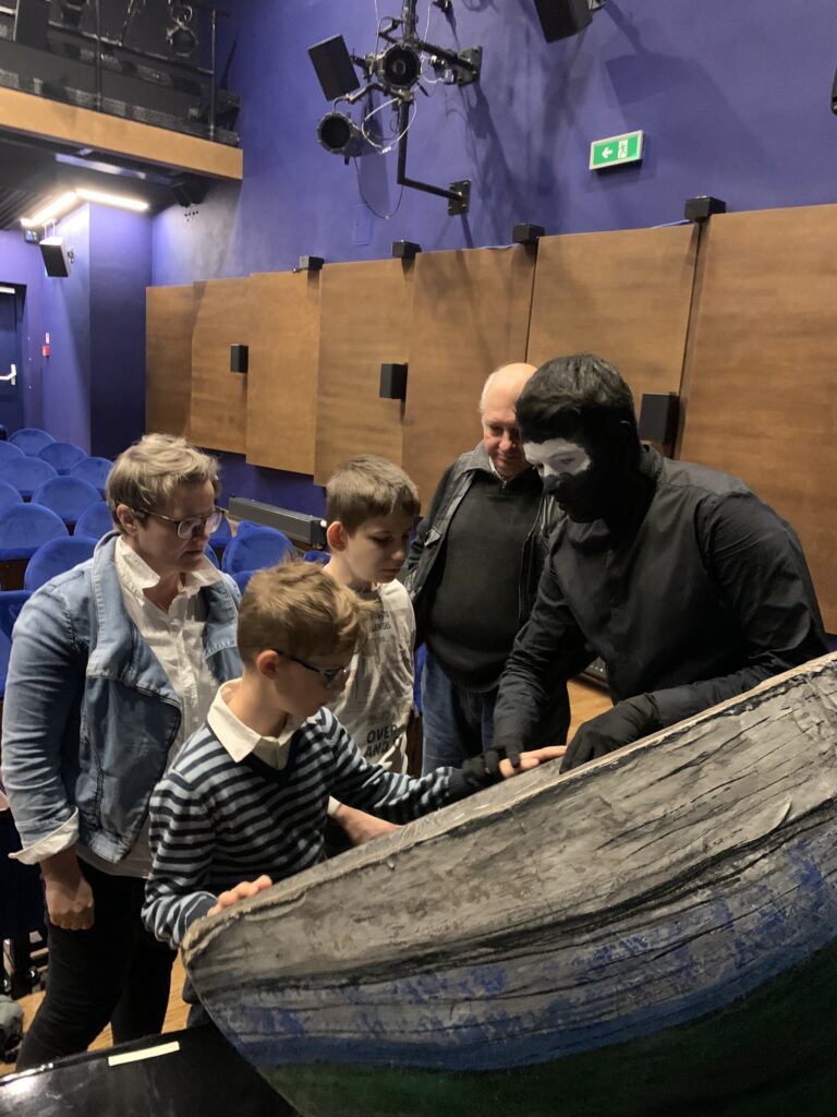 Aktor pokazuje Piotrkowi i Oliwierowi łódkę.