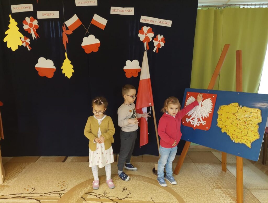 Troje dzieci przy symbolach patriotycznych.