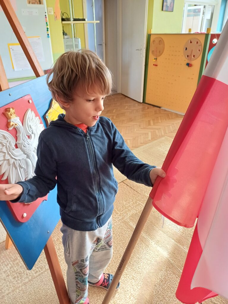 Chłopiec stoi przy dużej materiałowej fladze Polski.