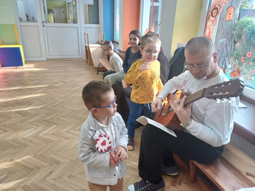 Dwóch chłopców przy panu terapeucie grającym na gitarze.