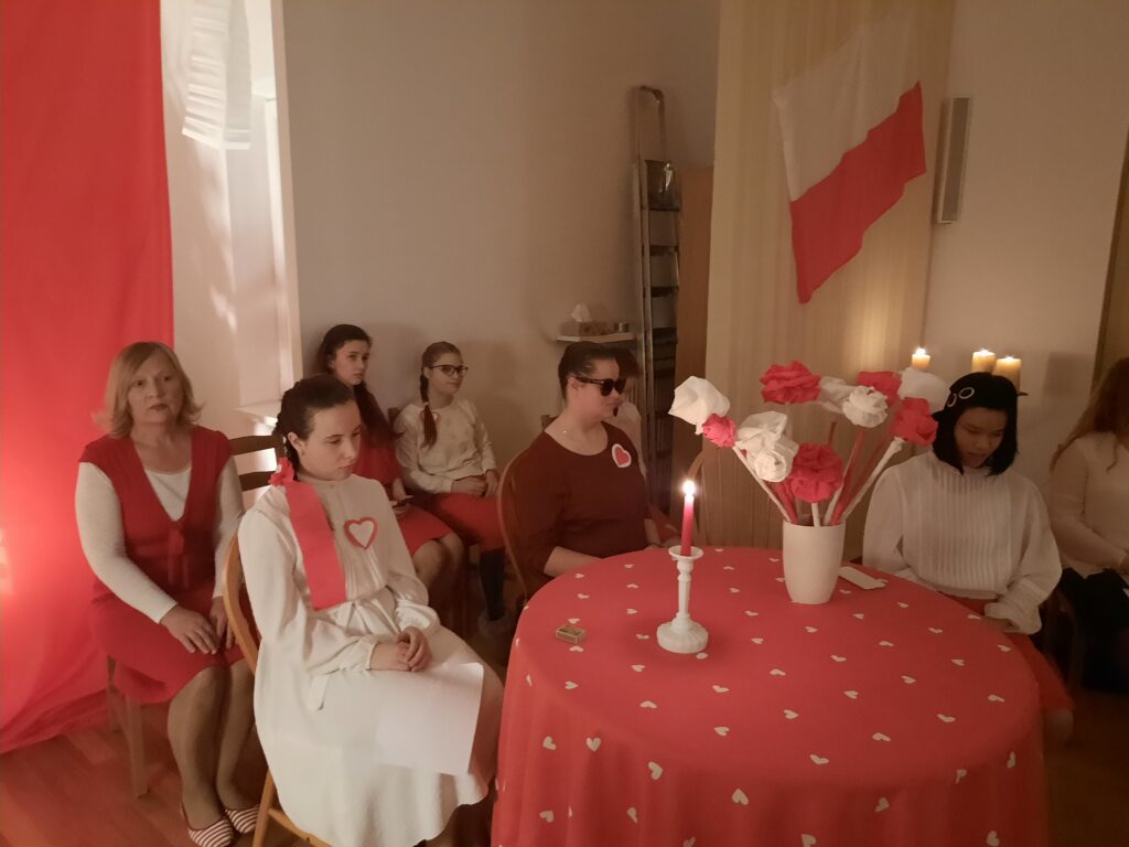 Odświętnie ubrane dziewczęta z grupy V siedzą na krzesłach z wychowawczynią panią Jolą 