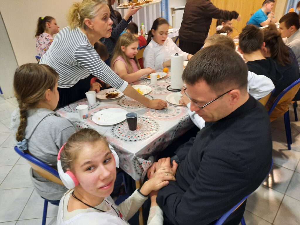 Ksiądz Marek siedzi przy stole w towarzystwie wychowanek