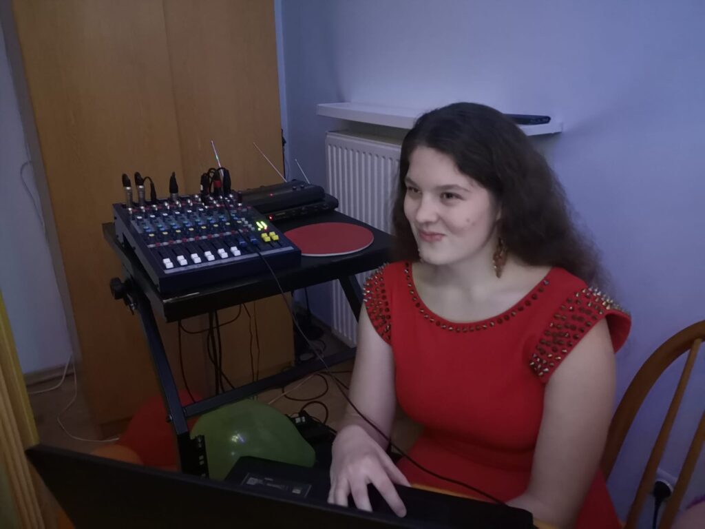 Wychowanka Ewa ubrana w czerwoną sukienkę siedzi przy aparaturze i czuwa nad muzyką