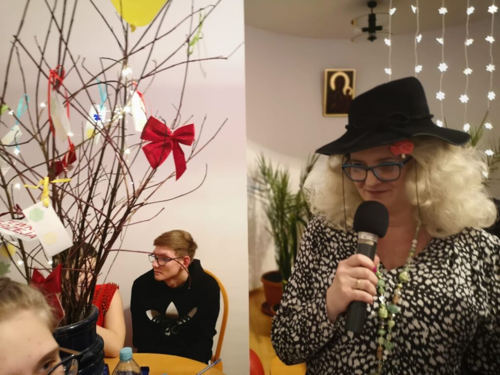 Pani Asia trzyma w ręku mikrofon i zaprasza do konkursu 8 odważnych dziewcząt