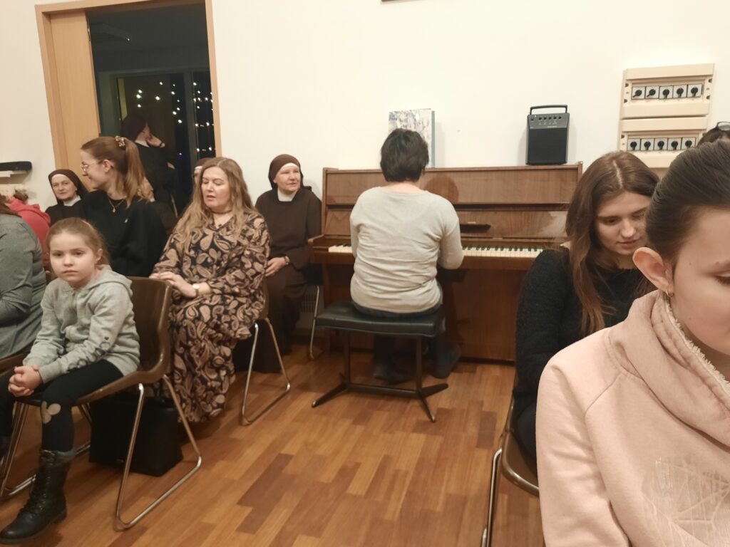 Uczestnicy kolędowania oraz Ewa  grająca na pianinie