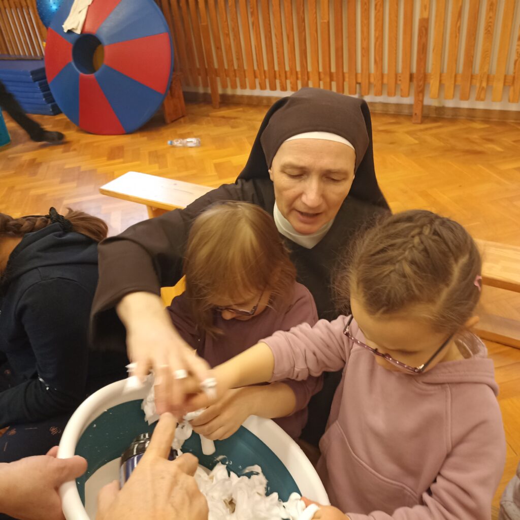S. Hiacynta z dziewczynkami zanurzają ręce w misce pełnej piany.
