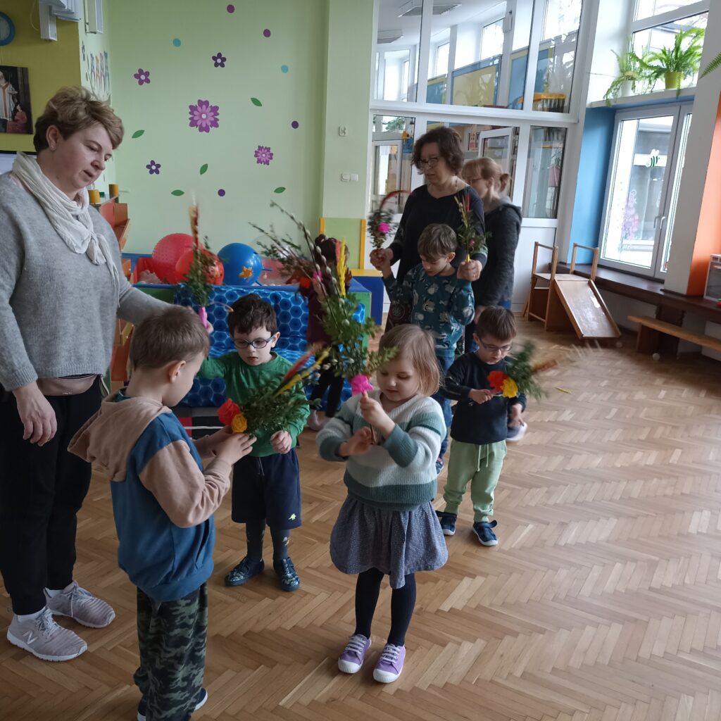 Dzieci i Panie z palmami w dłoniach na bawialni przedszkolnej.