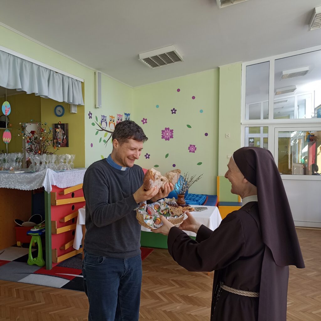 Ksiądz przełamuje chleb, s. Hiacynta podtrzymuje koszyk pod chlebem.