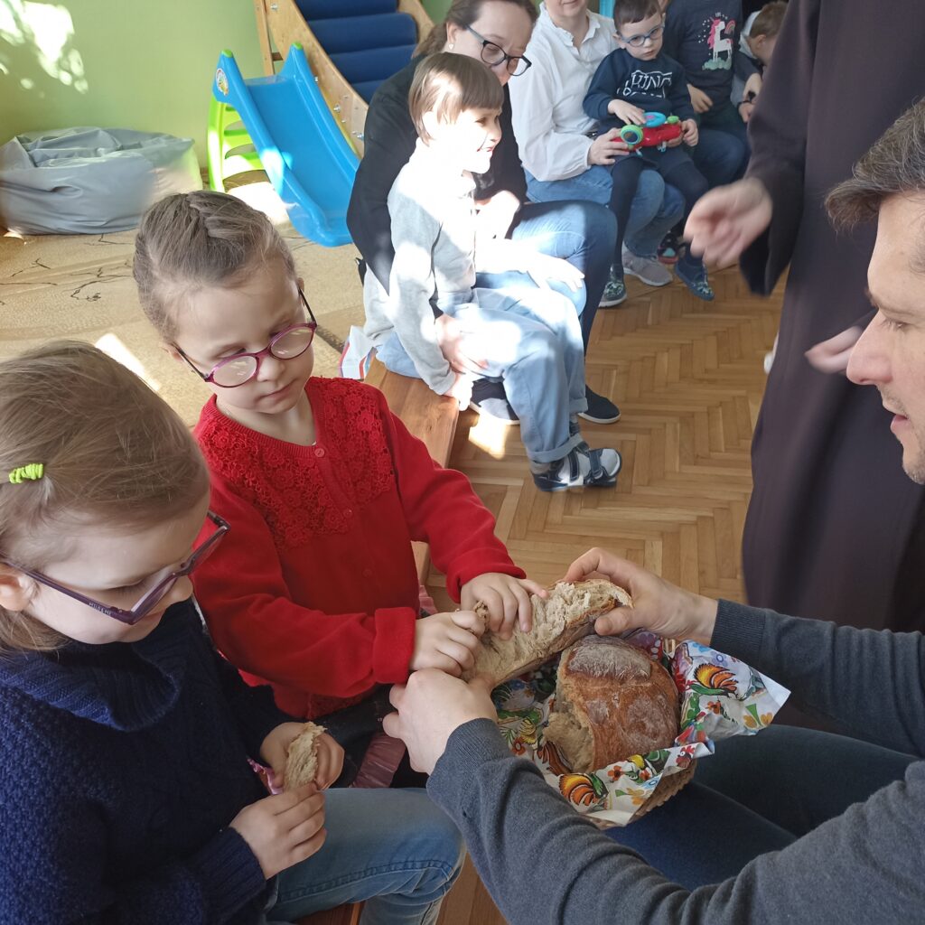 Ksiądz podaje dziewczynkom chleb.
