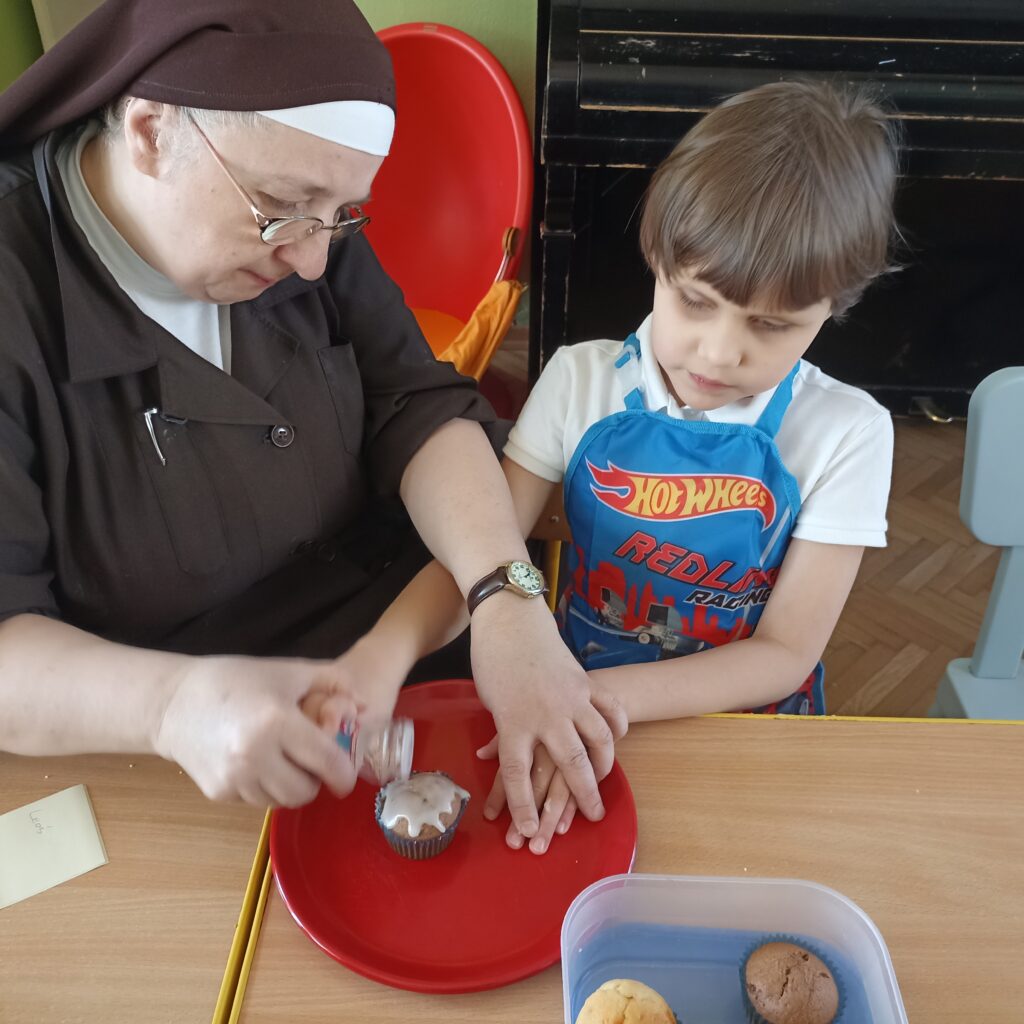 Chłopiec z s. Adrianą dekorują babeczkę.