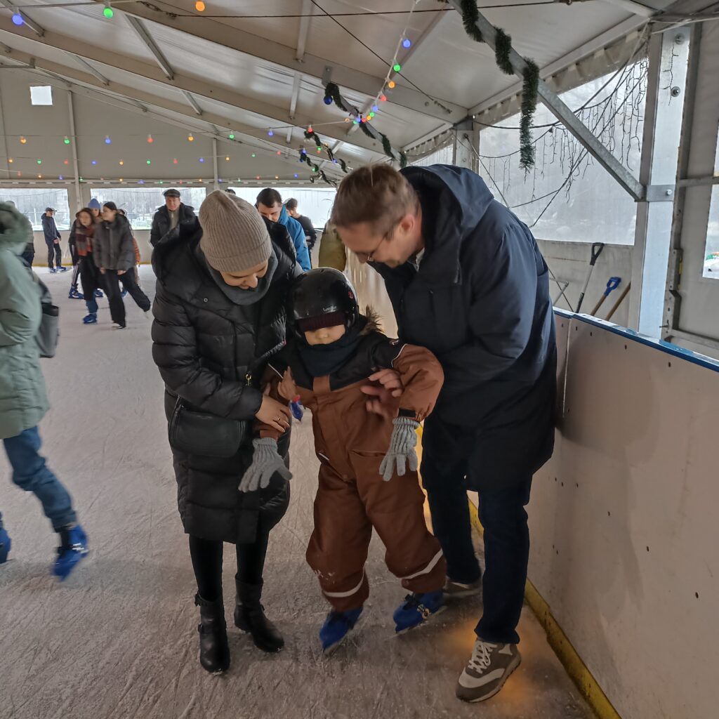 Chłopiec z pomocą rodziców jedzie na łyżwach