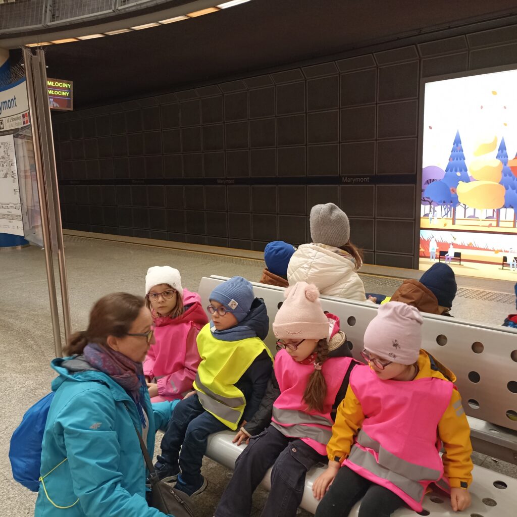 Przedszkolaki siedzą na ławce na peronie metra.