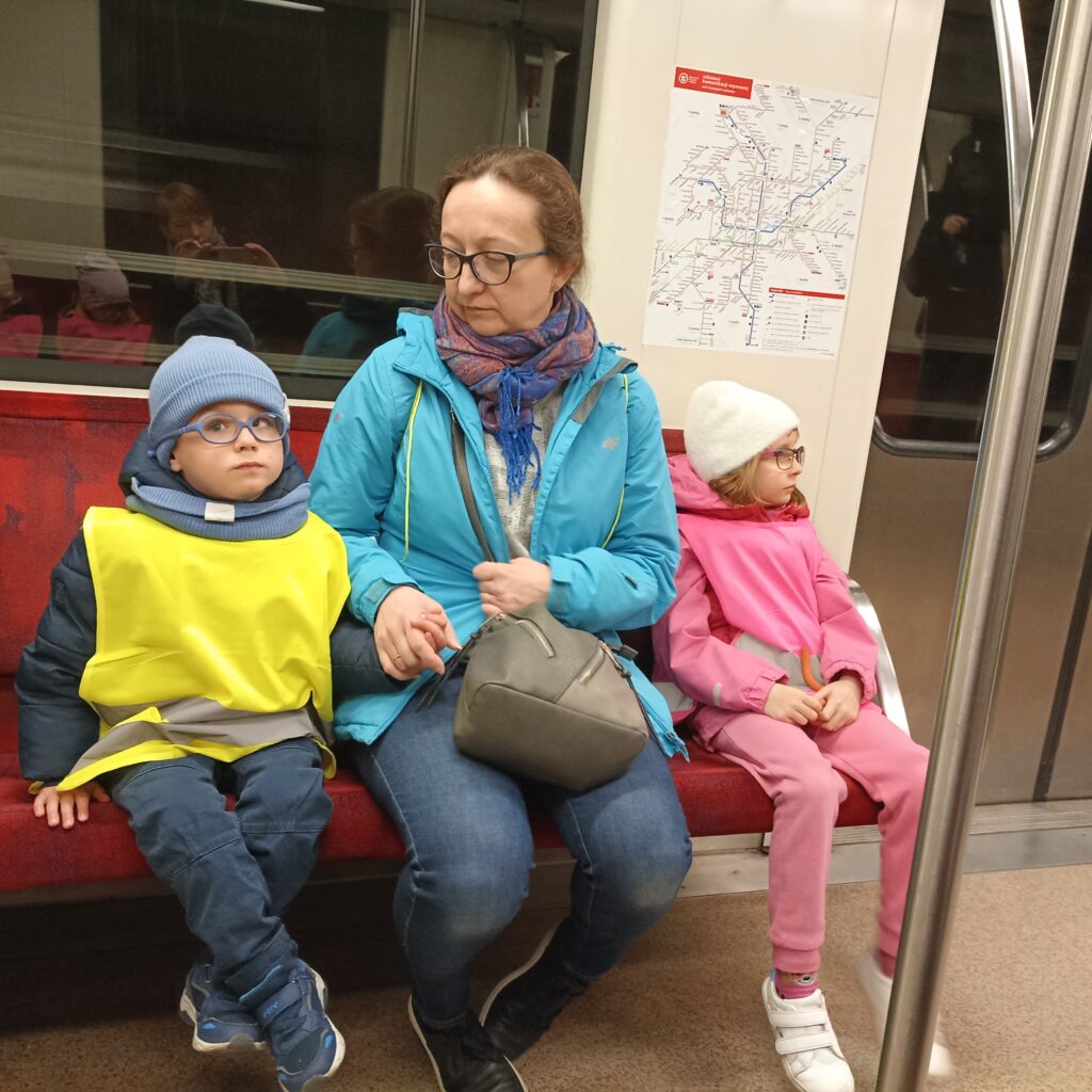 Przedszkolaki z wychowawczynią siedzą w środku wagonu metra.