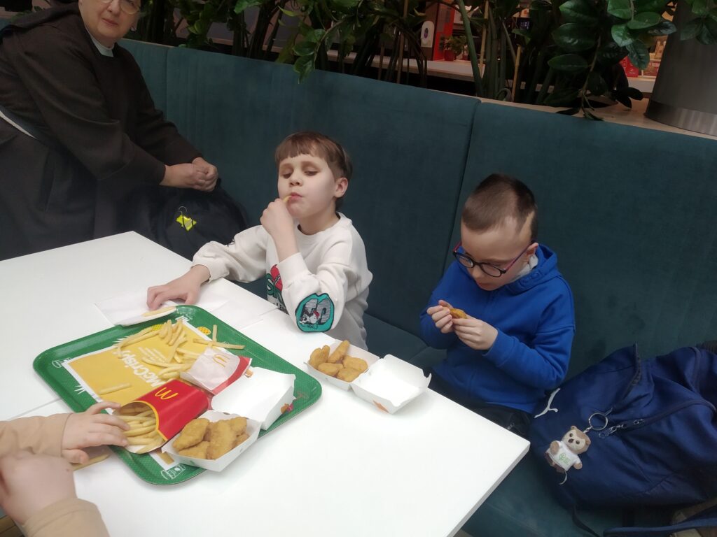 Przedszkolaki siedzą przy stole, na którym jest jedzenie z Mc. Donalds'a