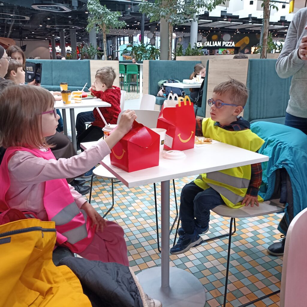 Przedszkolaki siedzą przy stole, na którym jest jedzenie z Mc. Donalds'a