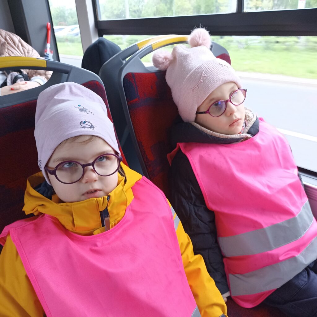 Dwie dziewczynki w kamizelkach odblaskowych siedzą na fotelach w autobusie