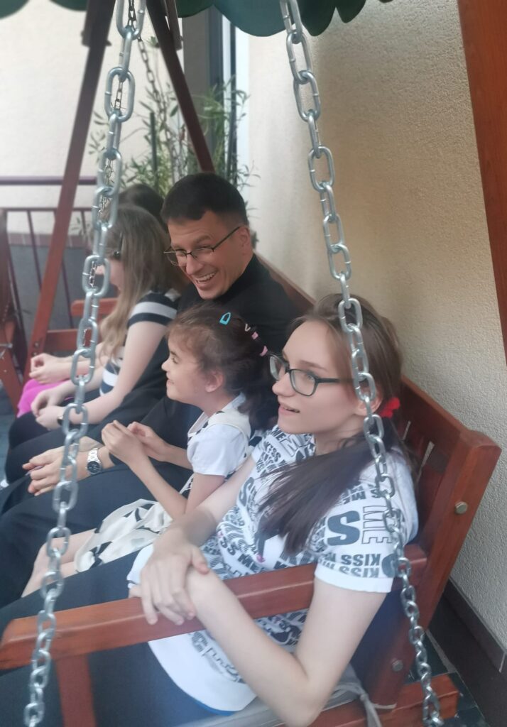 Ksiądz Marek z dziewczynkami na huśtawce ogrodowe