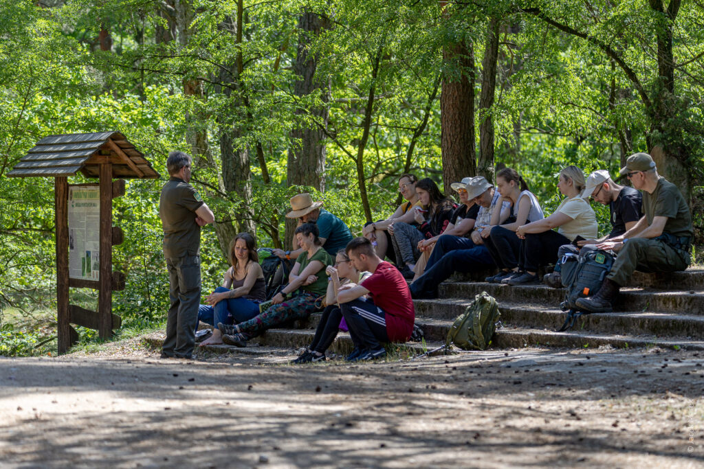 Grupa słucha prelekcji na ławkach.