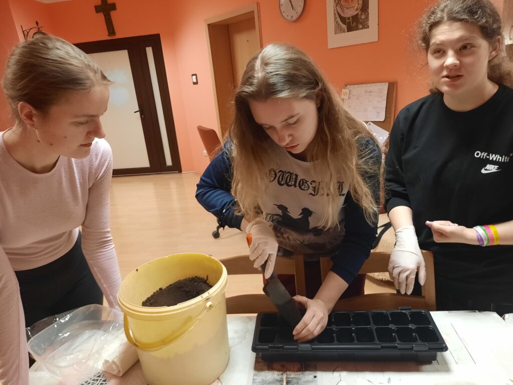 Dziewczęta  z grupy VI  przygotowują pojemniki z ziemią do posiania nasion