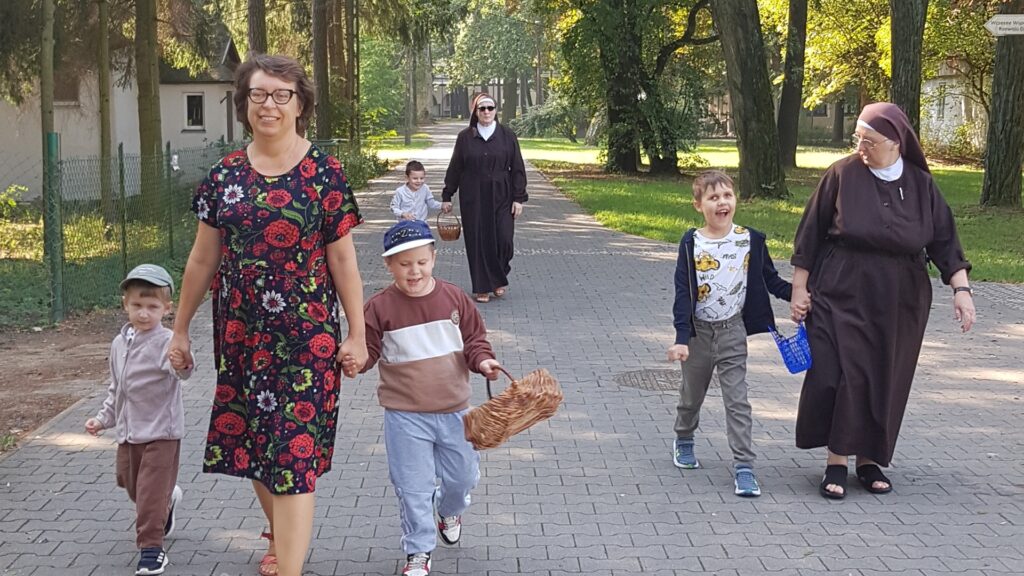 Dzieci i nauczyciele idą z koszykami do sadu.