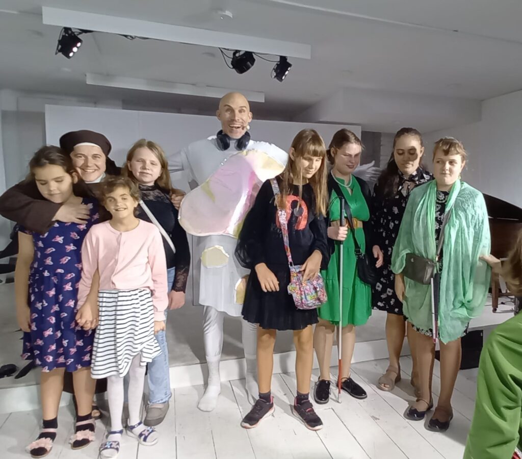 Aktor kleks w  białym stroju   i uczestnicy opery 