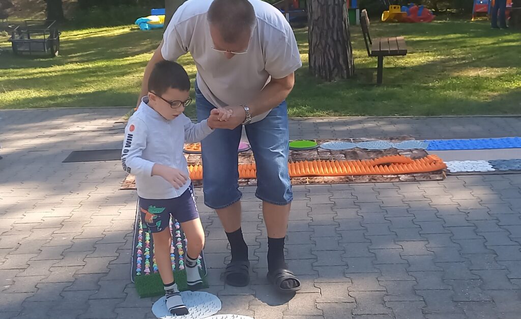 Rehabilitant pomaga chłopcu przejść po ścieżce sensorycznej.