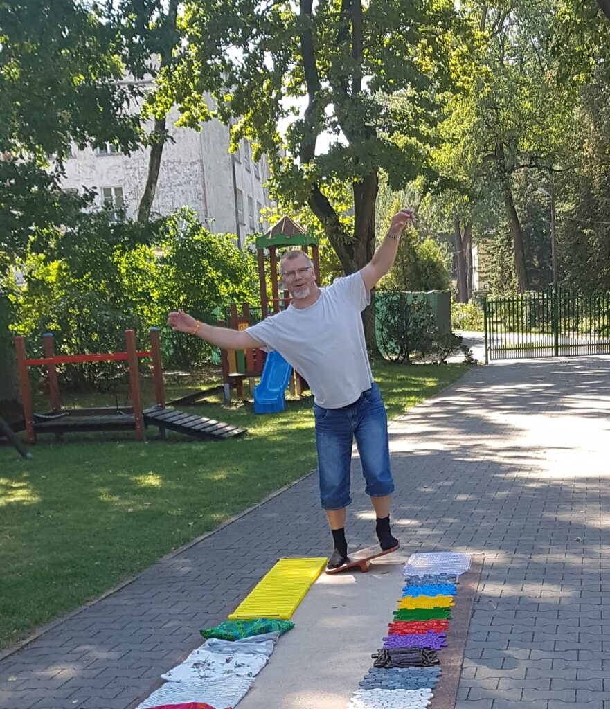 Rehabilitant z rękoma rozłożonymi na boki próbuje złapać równowagę na równoważni.