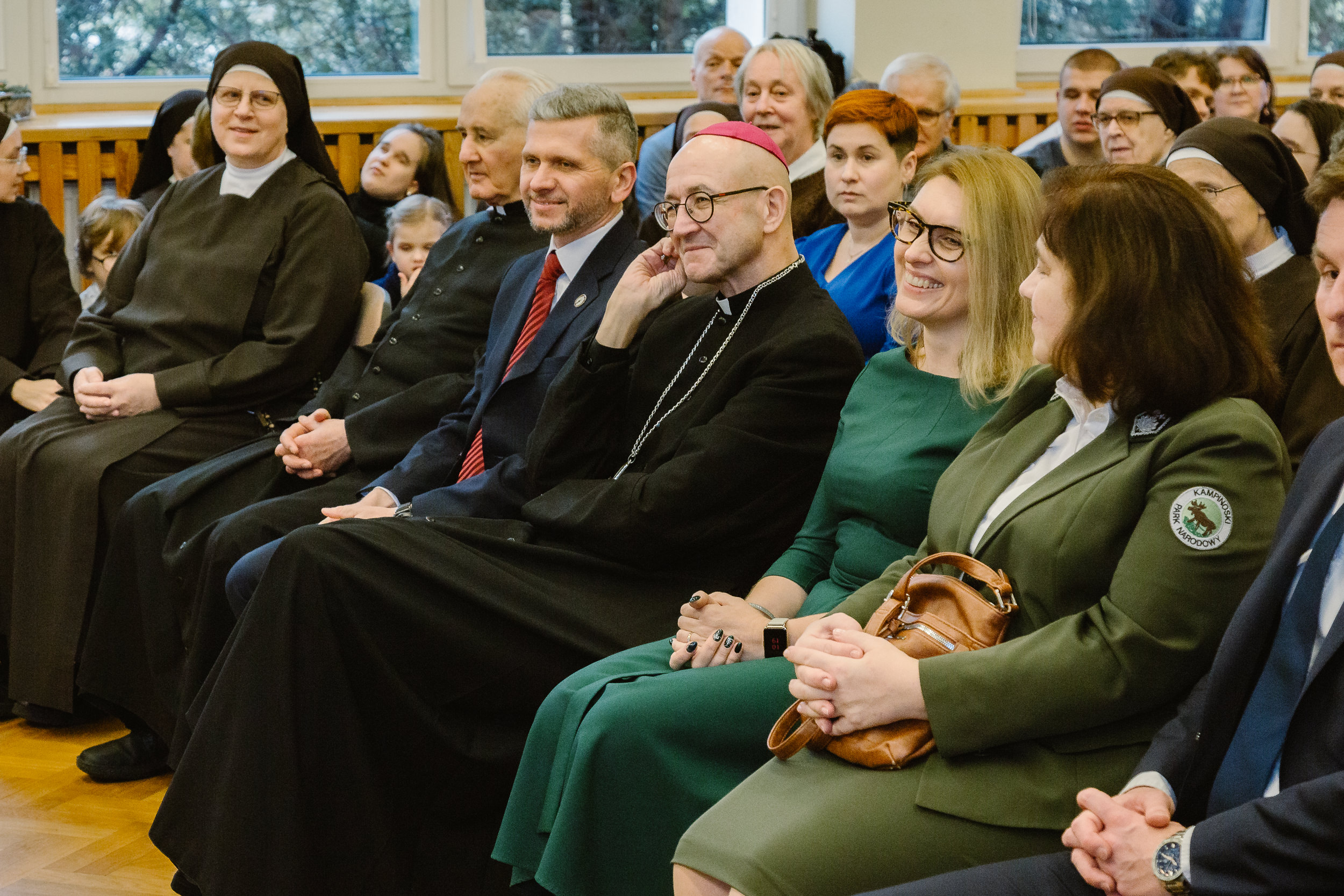Arcybiskup Adrian Galbas na sali gimnastycznej z prezesem, dyrektor Ośrodka i dyrektor szkoły podstawowej.