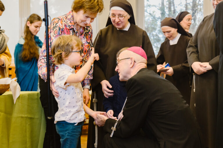 Arcybiskup kuca i rozmawia z jednym z przedszkolaków.