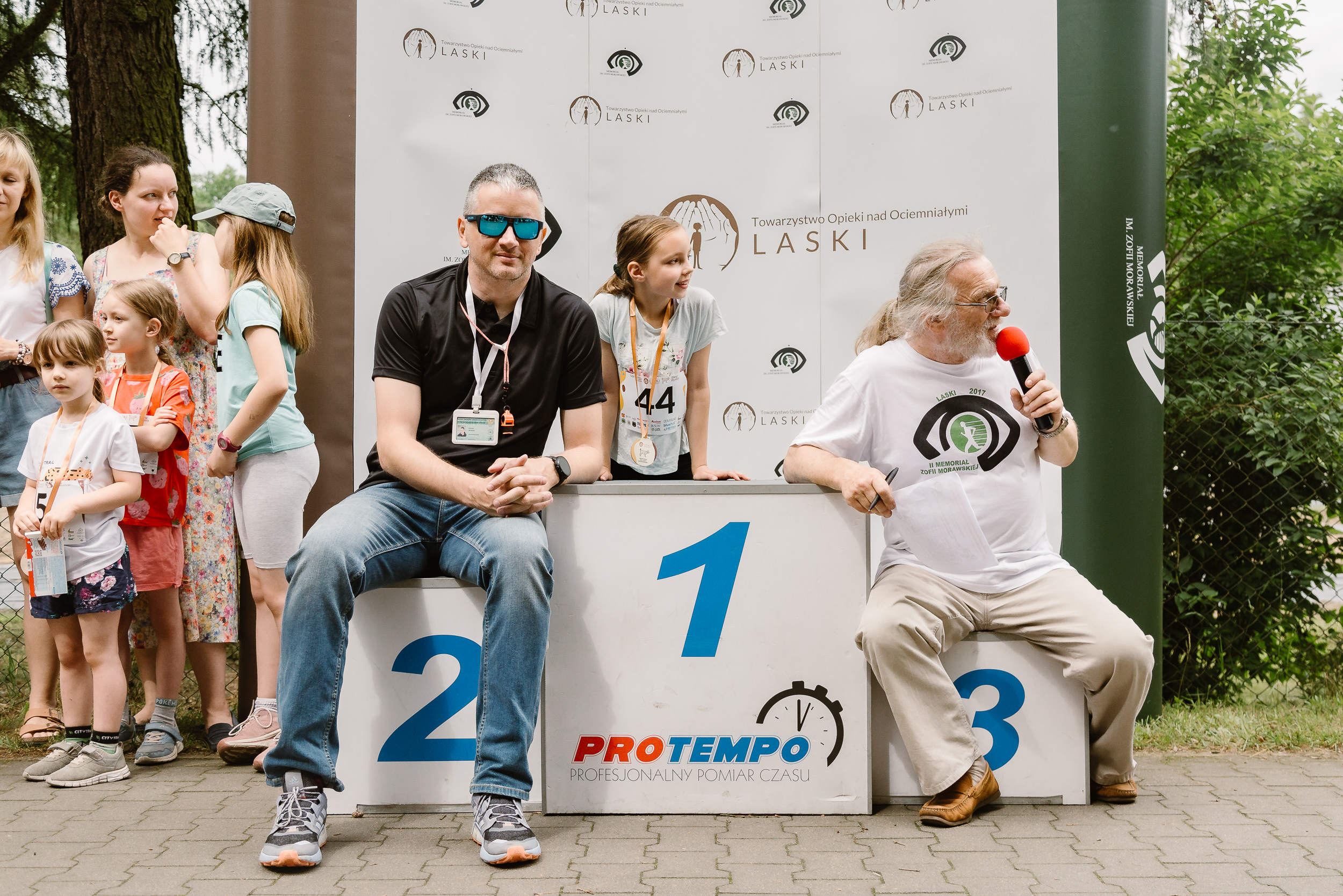 Na stopniach podium siedzą Daniel z firmy obsługującej pomiar czasu oraz Stanisław Badeński, który w tym roku był konferansjerem.