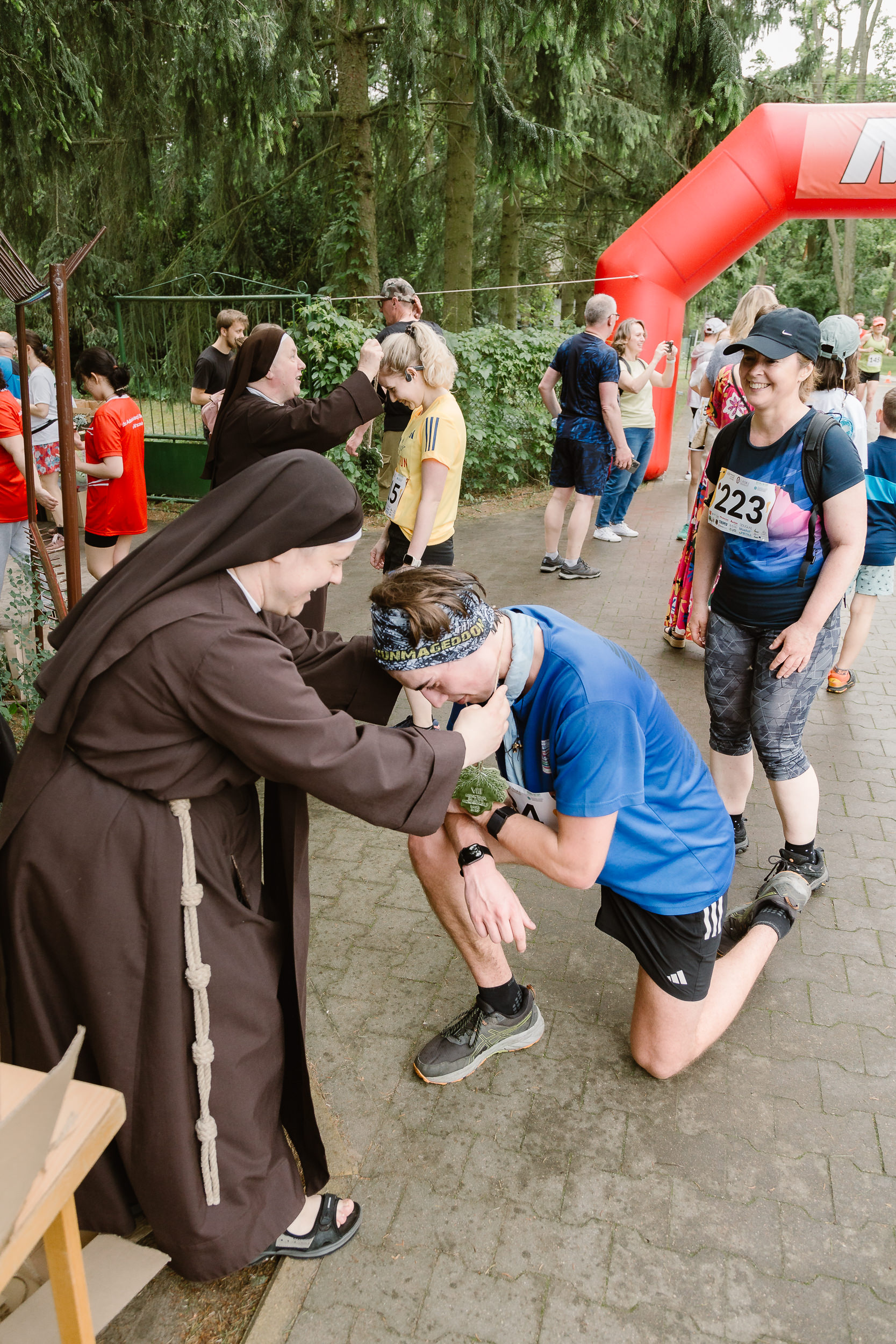 Biegacz klęczy przed franciszkanką, która zakłada mu na szyję medal.