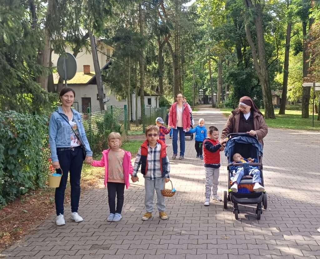 Przedszkolaki i nauczycielki z koszykami w dłoniach w drodze do sadu.