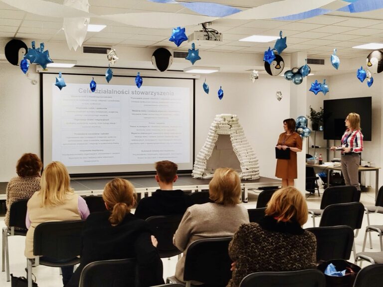 siedzące osoby na sali oglądające prezentację na ekranie rzutnika