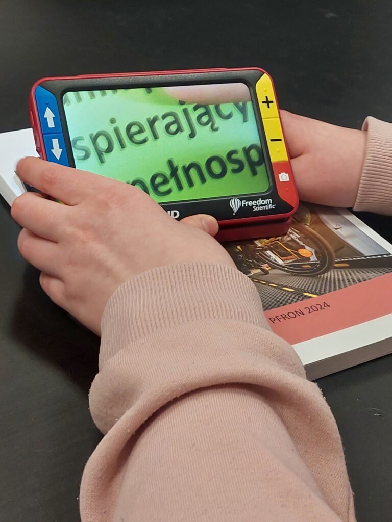 uczeń próbuje czytać okładkę książki przez mobilny powiększalnik elektroniczny