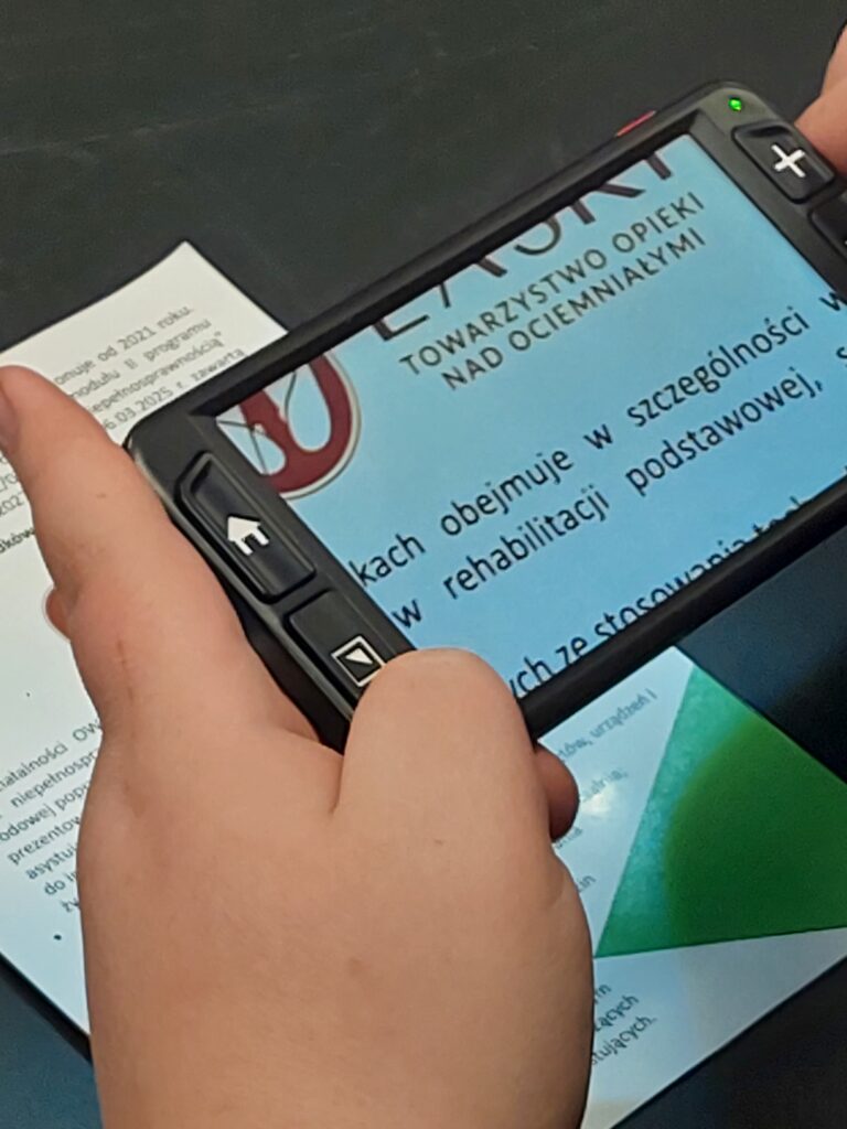 uczeń próbuje czytać okładkę książki przez mobilny powiększalnik elektroniczny