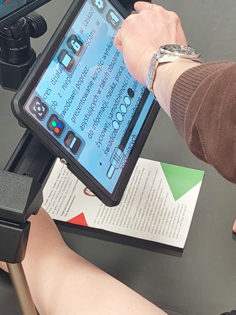 pracownik dostosowuje powiększalnik stacjonarny do możliwości odczytu przez ucznia